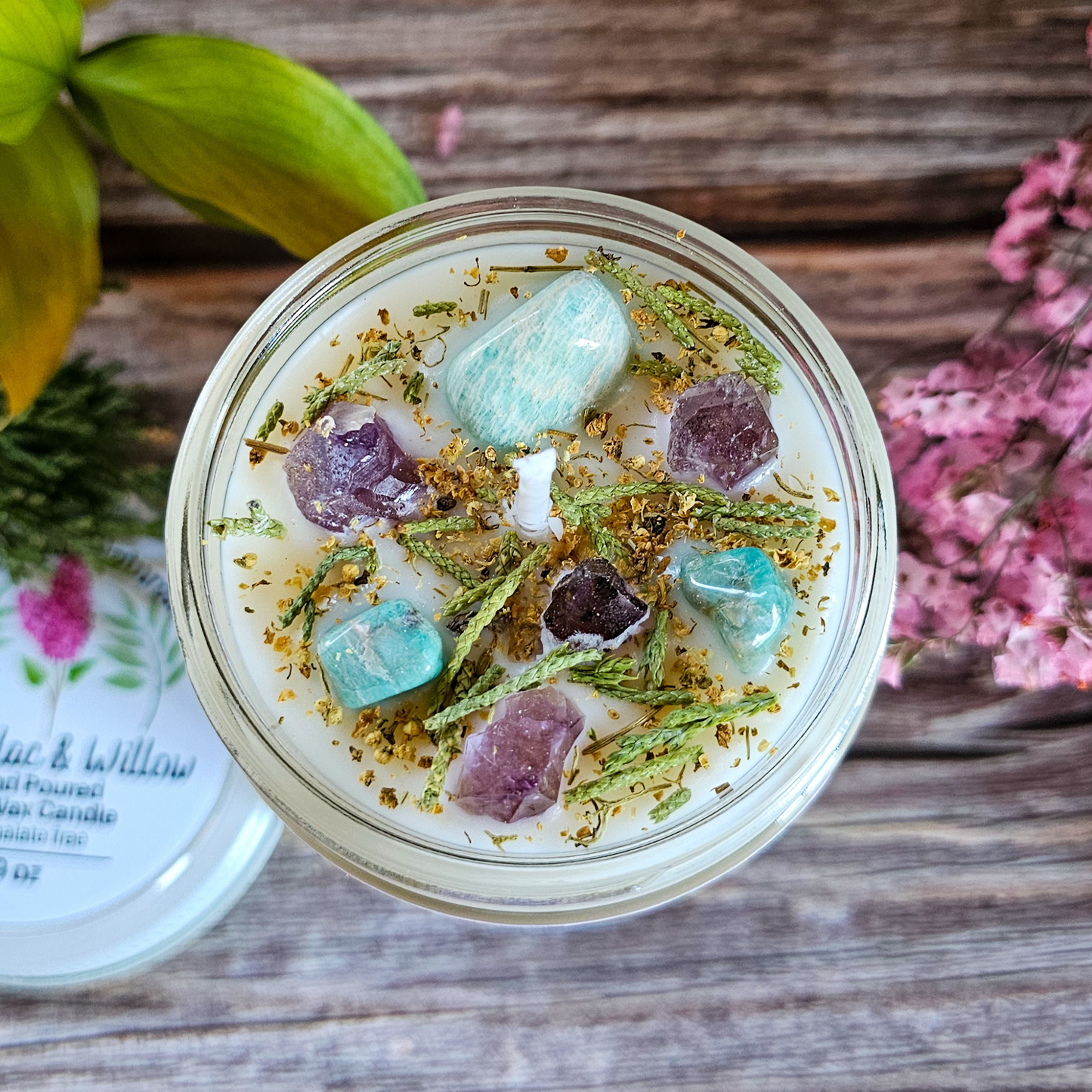 Jar with decorative stones and herbs on a wooden surface with flowers in the background