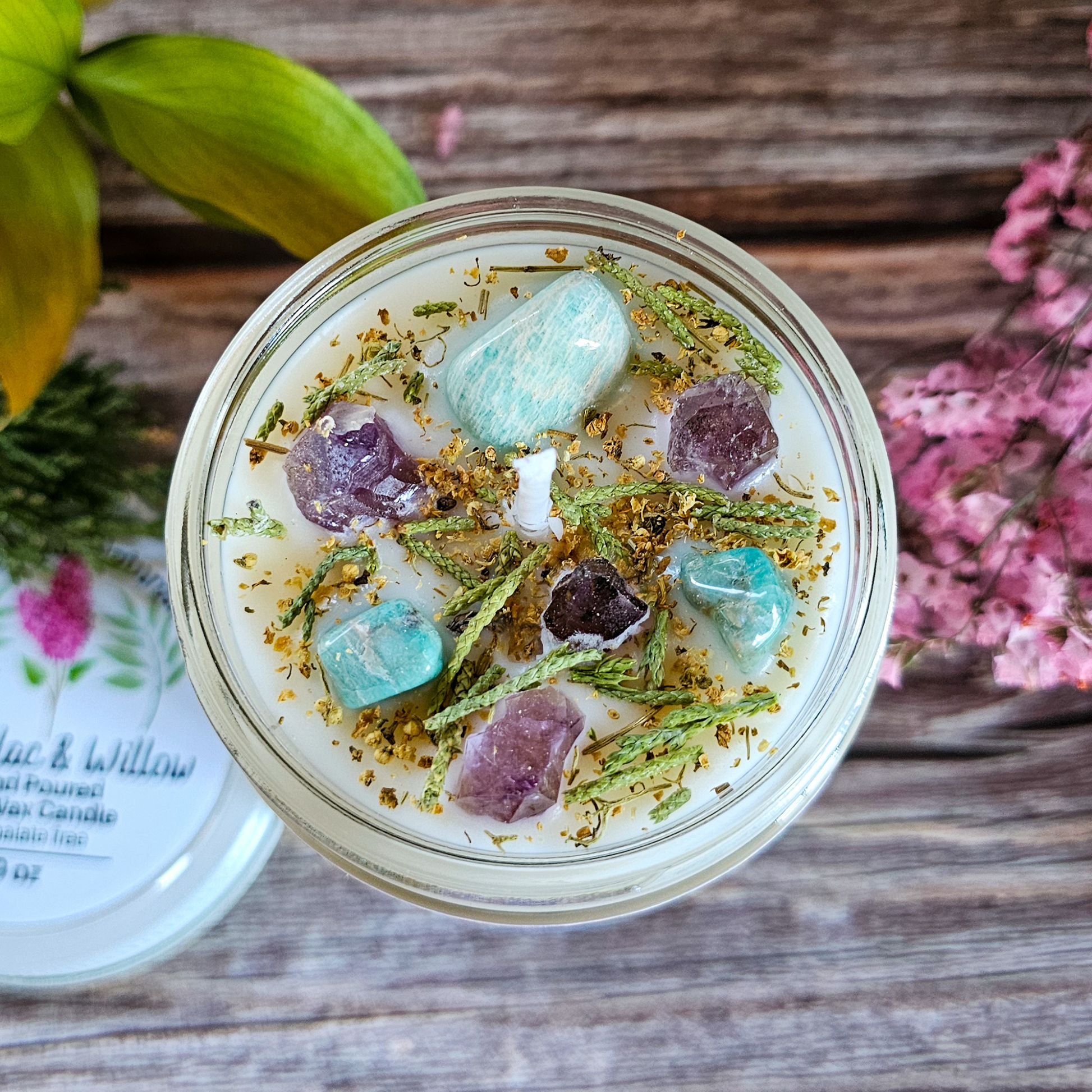 Jar with decorative stones and herbs on a wooden surface with flowers in the background