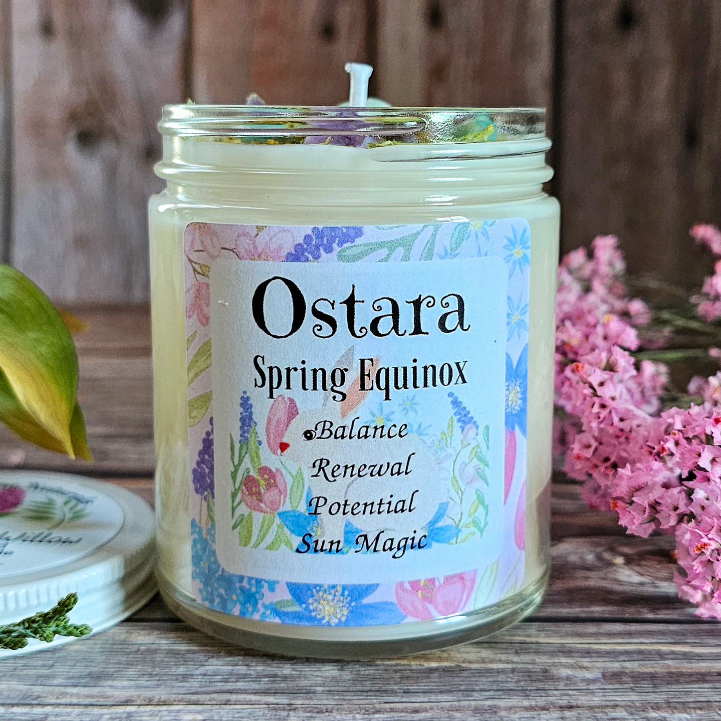 Candle jar labeled 'Ostara Spring Equinox' with floral design on a wooden surface.