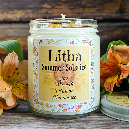 Candle with 'Litha Summer Solstice' label surrounded by flowers on a wooden surface