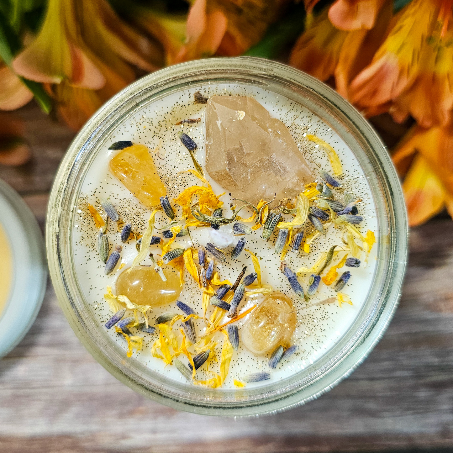 Glass jar with decorative elements on a wooden surface with flowers in the background