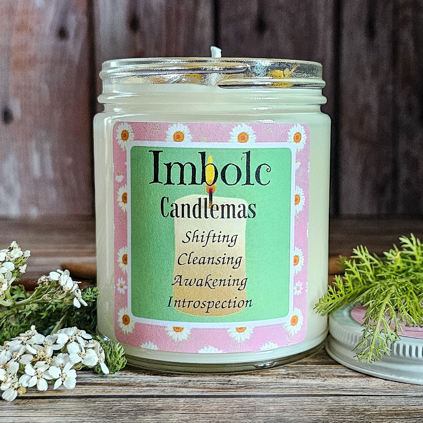 Candle with 'Imbolc Candlemas' label on a wooden surface with greenery