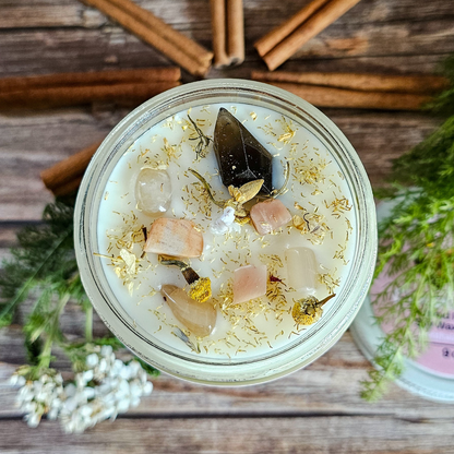 Glass jar with decorative stones and crystals on a wooden surface with cinnamon sticks and greenery.