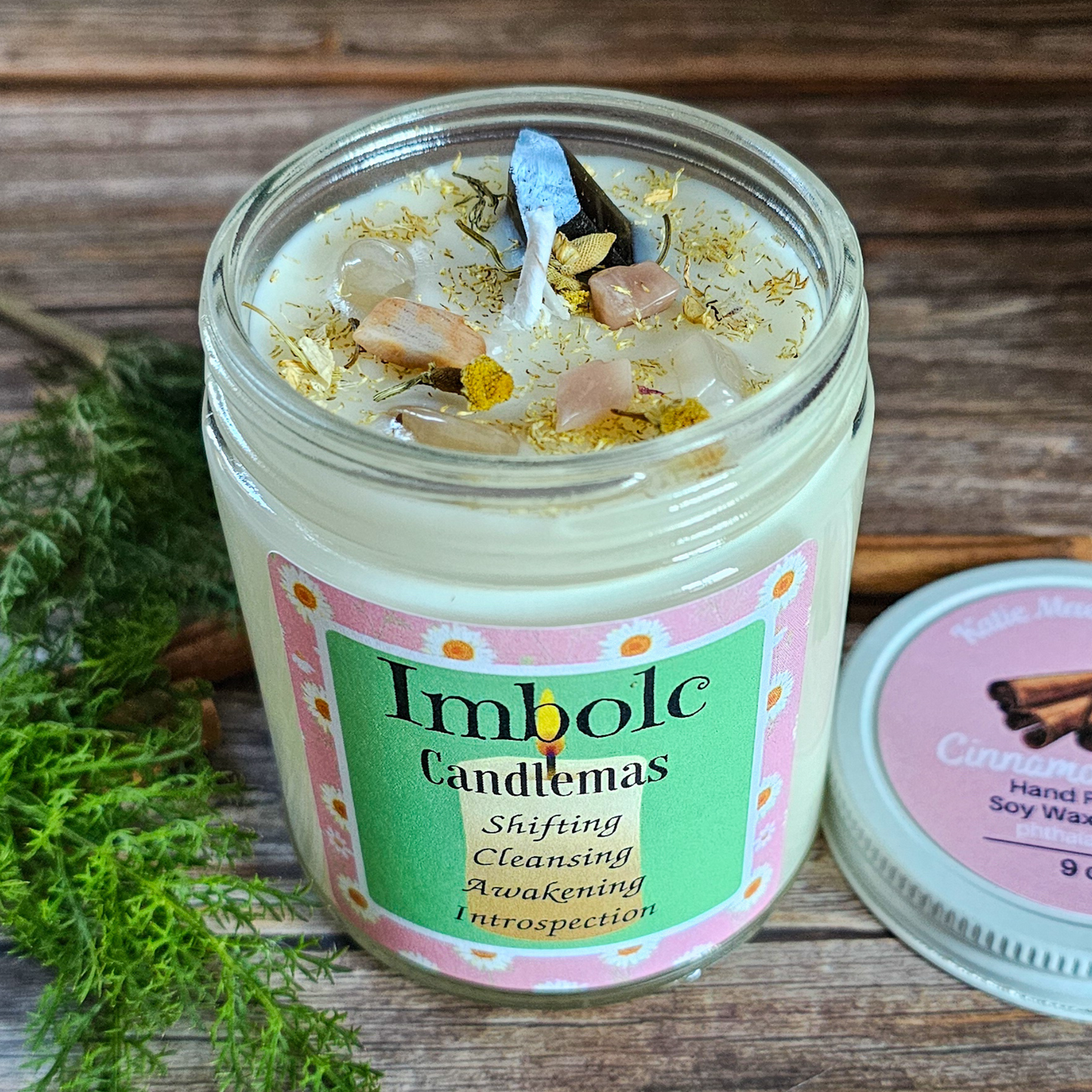 Candle in a glass jar with an Imbolc Candlemas label on a wooden surface.