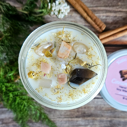 Candle in a glass jar with decorative elements on a wooden surface with cinnamon sticks and flowers.