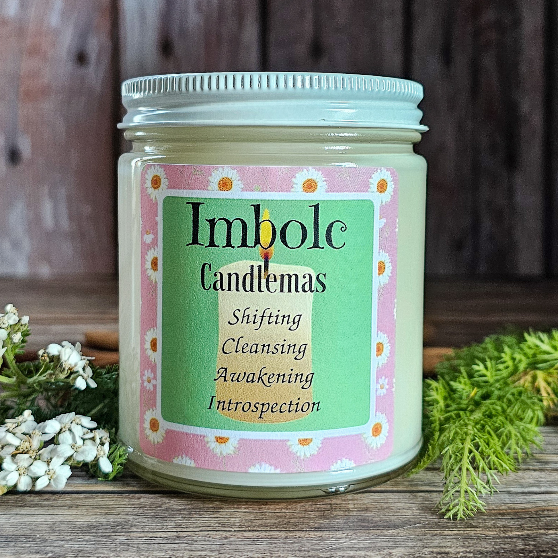 Candle jar labeled 'Imbolc Candlemas' on a wooden surface with natural elements.