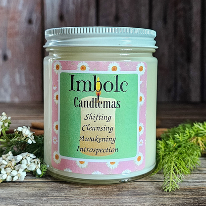 Candle jar labeled 'Imbolc Candlemas' on a wooden surface with natural elements.