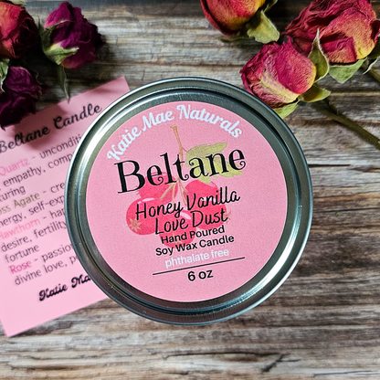 Beltane Honey Vanilla Love Dust candle on a wooden surface with flowers and a card.