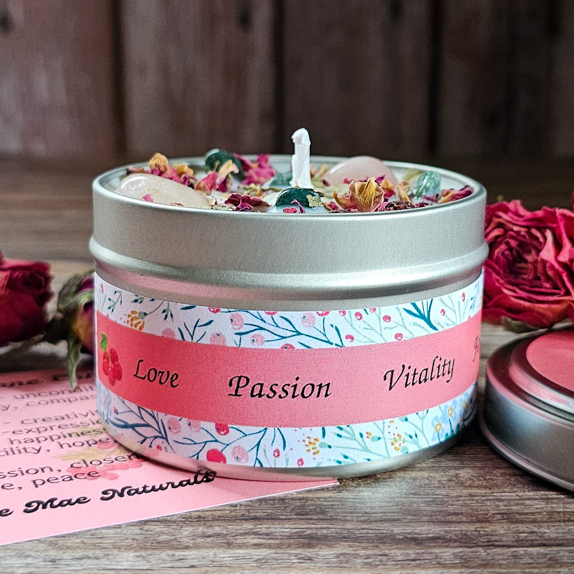 Candle in a tin with decorative label on a wooden surface with flowers.