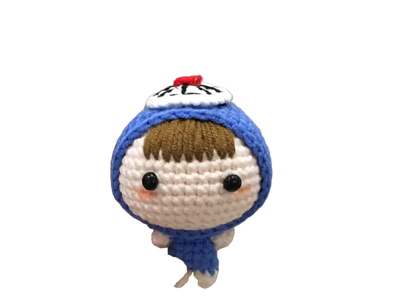 Hand holding a small crocheted character with a blue outfit and brown hair against a neutral background.