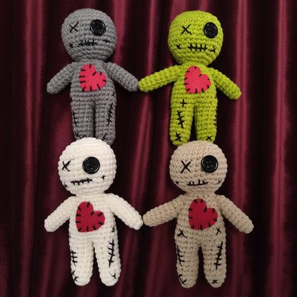 Four crocheted dolls with heart designs on their chests against a gray background
