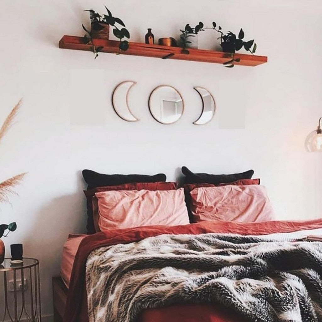 Neatly made bed with pink bedding and black pillows, wooden shelf with plants above, and decorative wall mirrors.