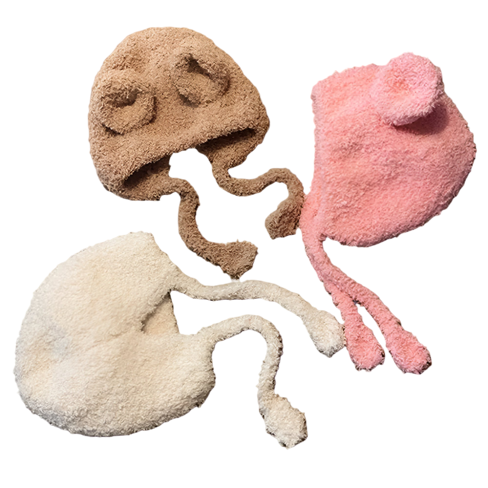 Three fuzzy animal-shaped hats in brown, pink, and white on a wooden surface.