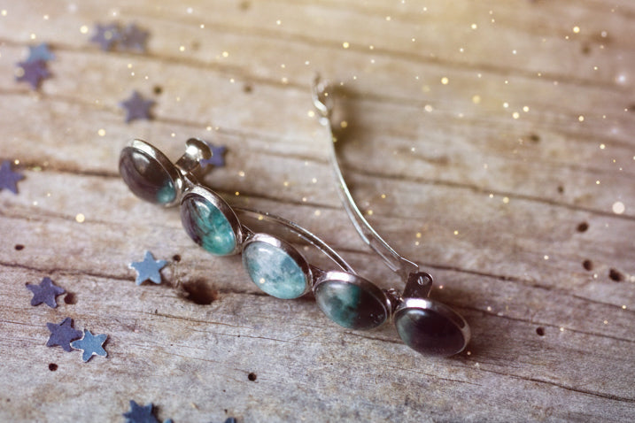 Silver brooch with green gemstones on a wooden surface with star-shaped objects.