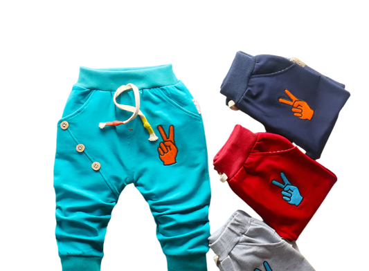 Colorful children's pants with peace sign designs on a woven mat.