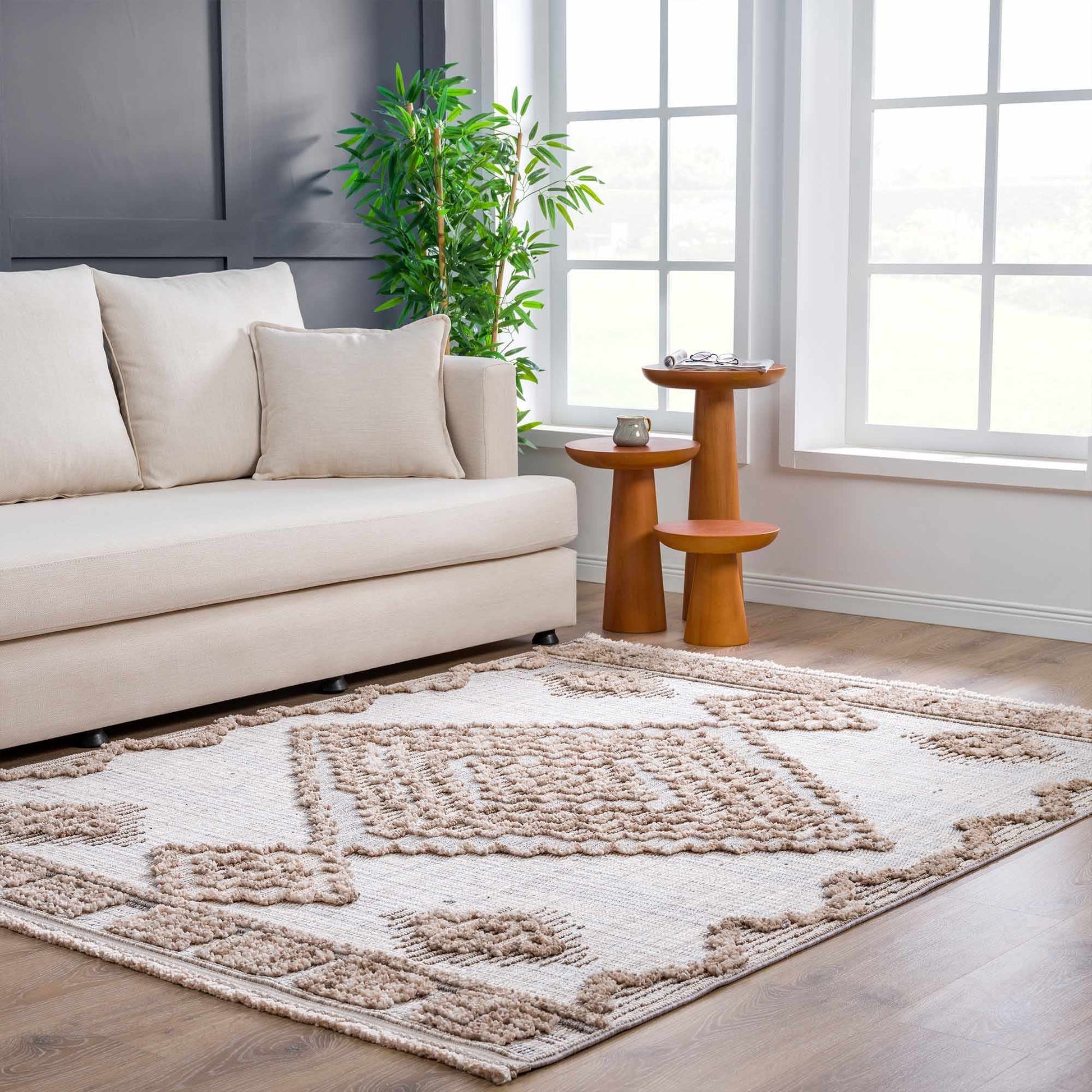 Beige sofa with decorative pillows on a patterned rug in a living room setting.