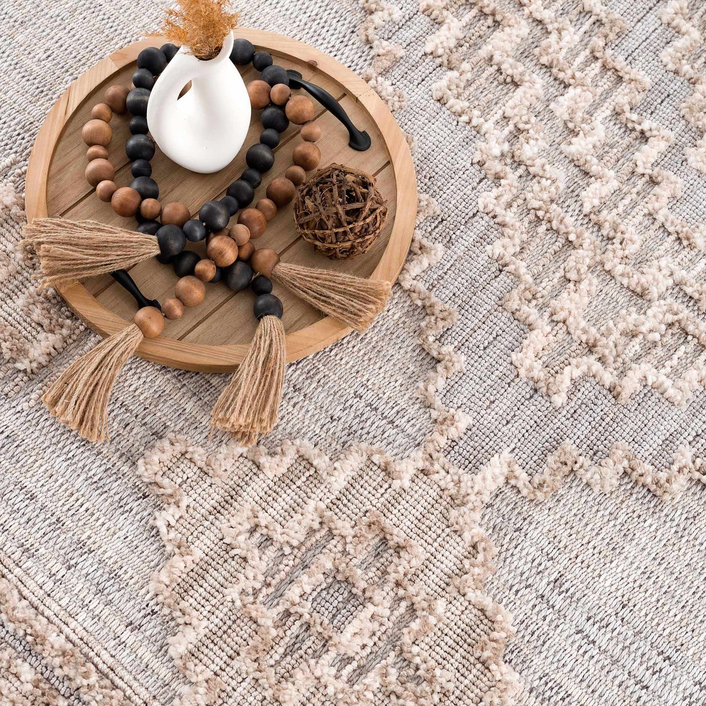 Decorative wooden tray with beads and a white vase on a textured surface