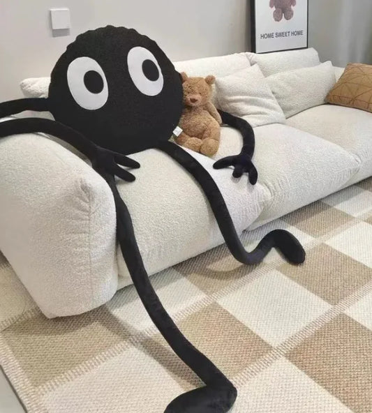 Large black spider plush toy on a white sofa with a teddy bear