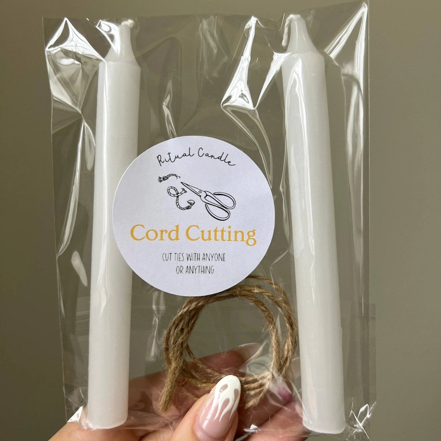 Two white candles in clear packaging with a label on a brown background