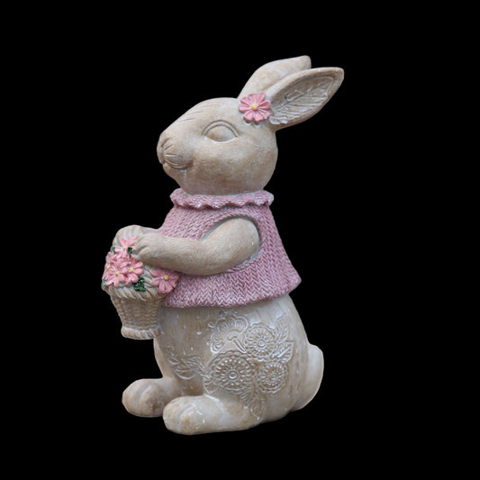 Decorative rabbit figurine wearing a pink sweater and holding flowers on a stone surface.