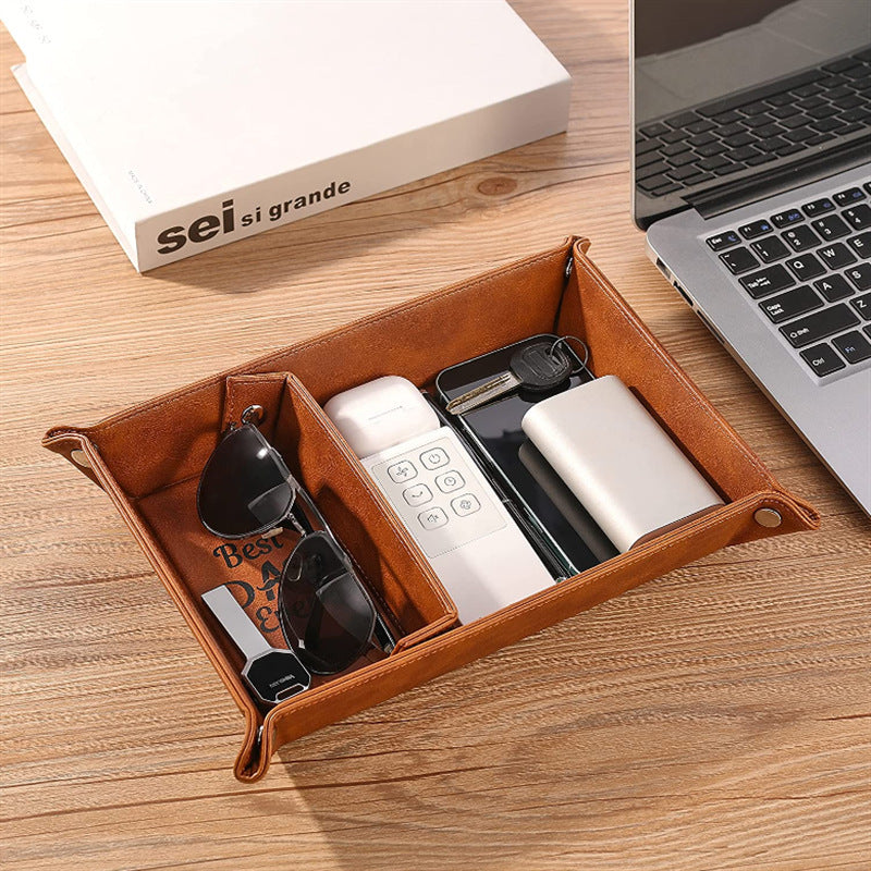Brown leather tray with small items on a wooden desk next to a laptop