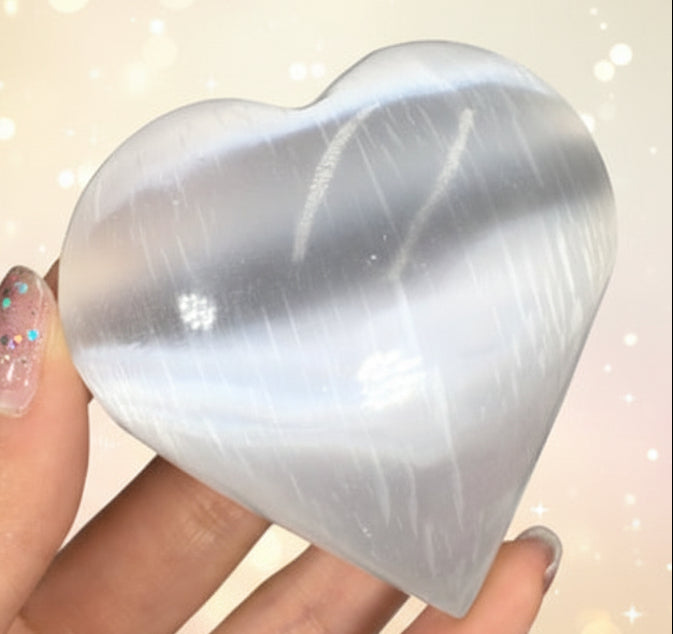 Heart-shaped crystal held by a hand with glittery nail polish against a dark background.