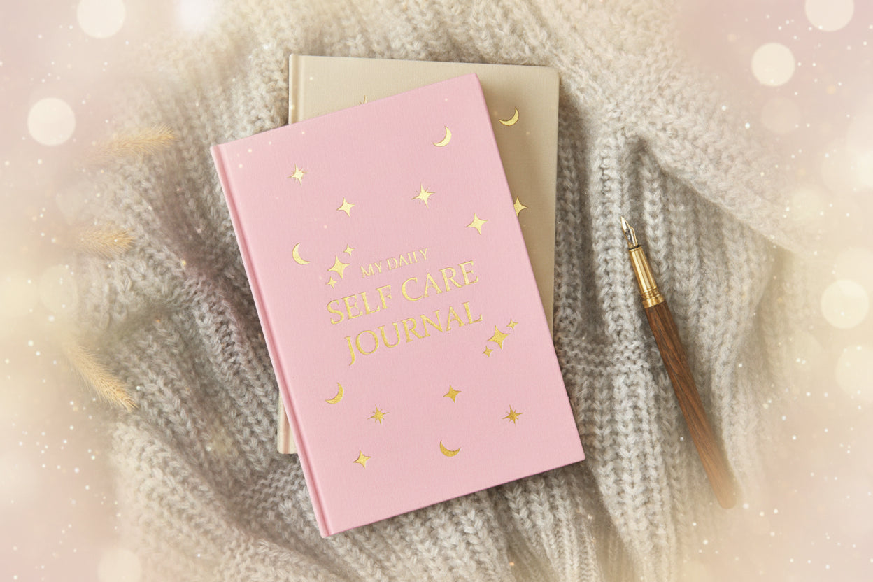 Pink 'Self Care Journal' with gold text and designs on a textured surface