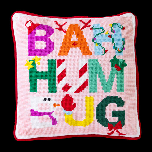 Decorative pillow with colorful letters spelling 'BAH HUM UG' on a pink background