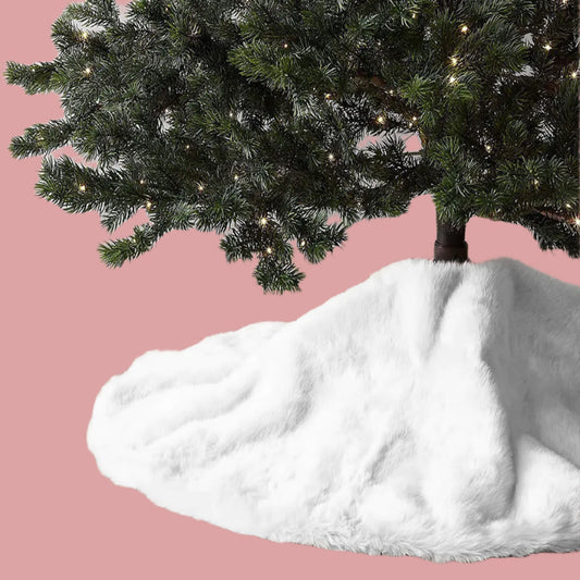 White fur tree skirt on a wooden floor with a decorated Christmas tree in the background.
