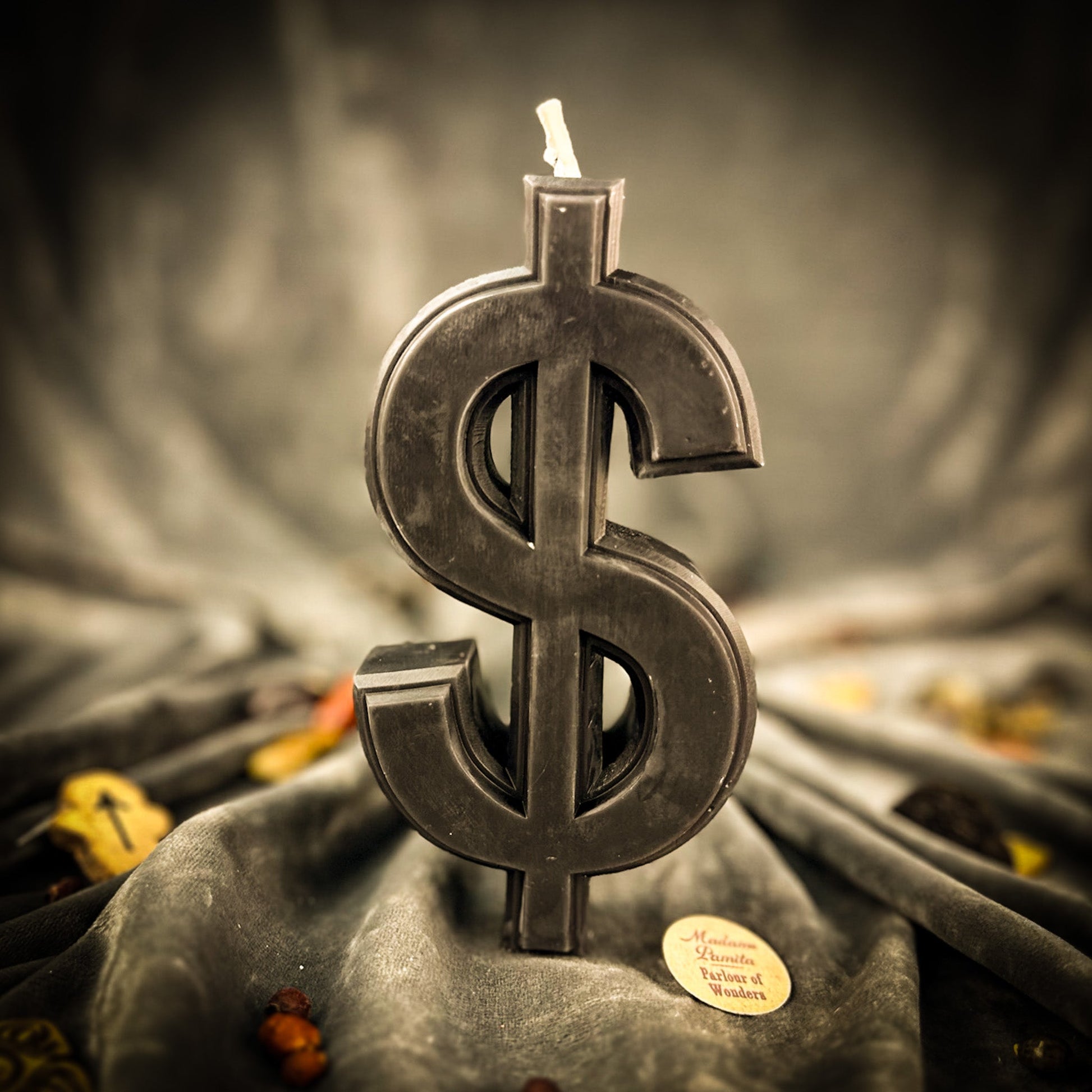 Candle shaped like a dollar sign on a dark fabric background