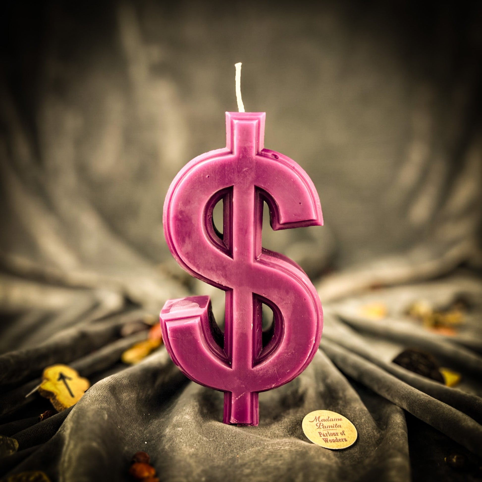 Pink dollar sign candle on a textured surface with a blurred background
