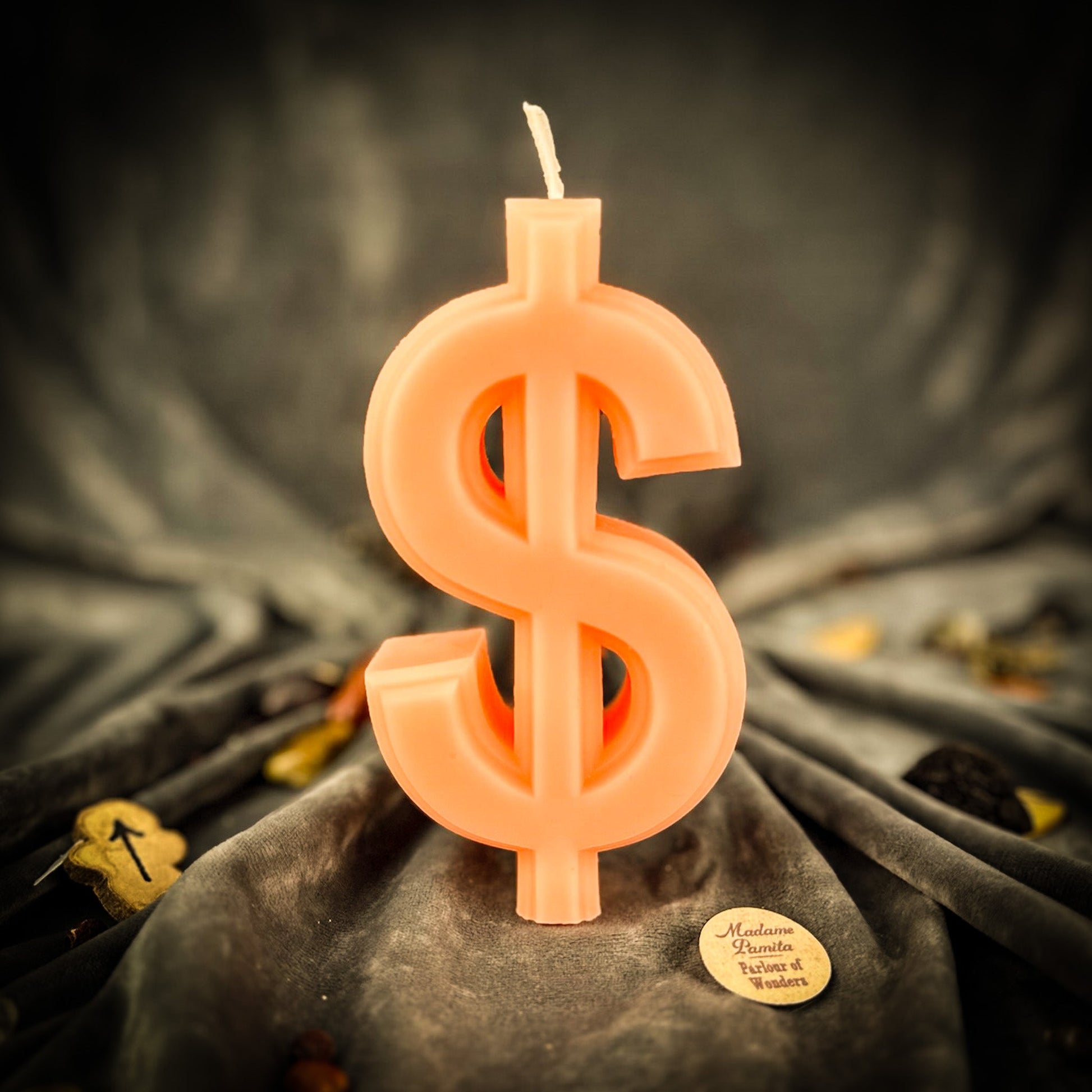 Candle shaped like a dollar sign on a dark fabric background