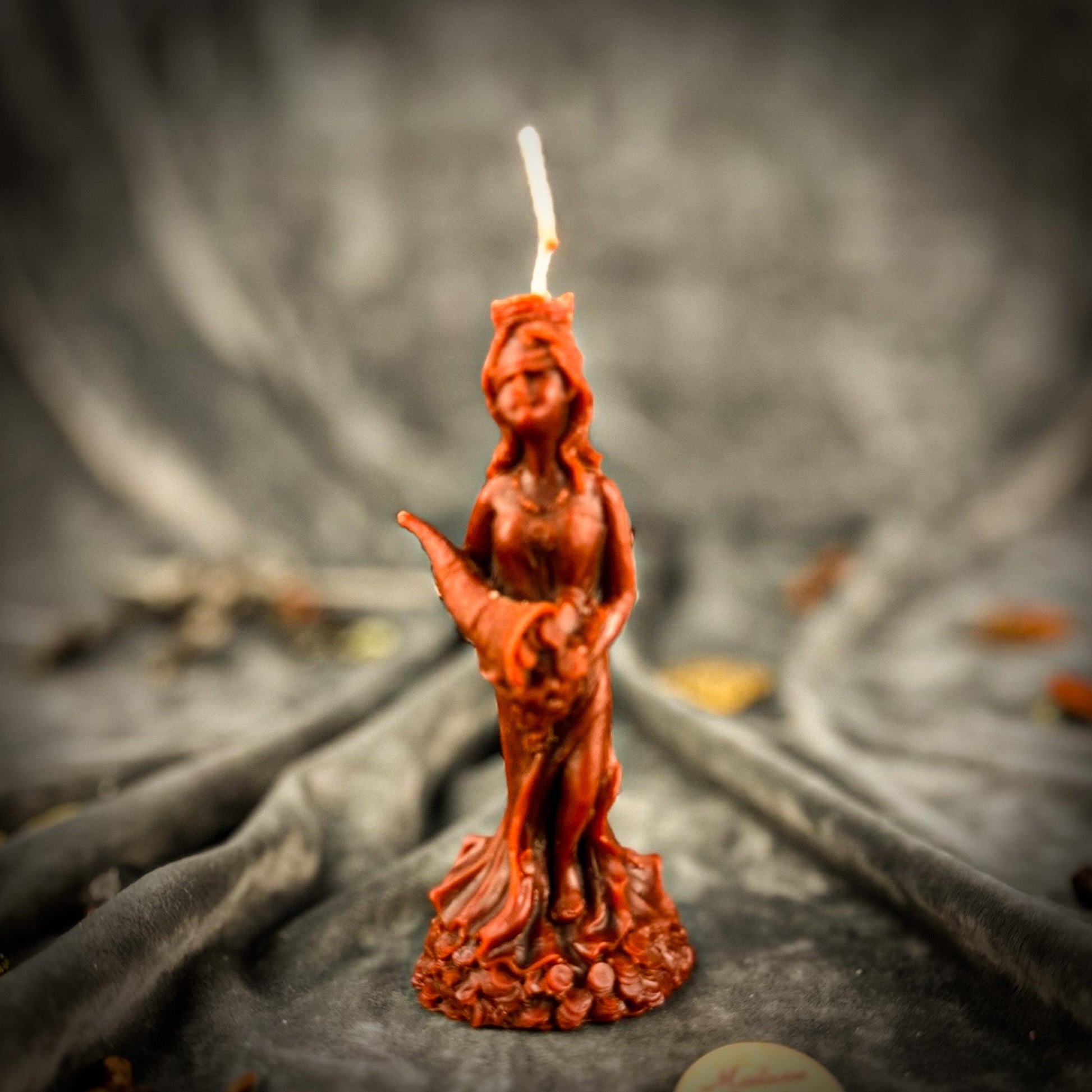 Red candle-shaped sculpture of a woman holding a candle on a dark fabric background