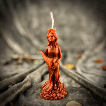 Red candle-shaped sculpture of a woman holding a candle on a dark fabric background