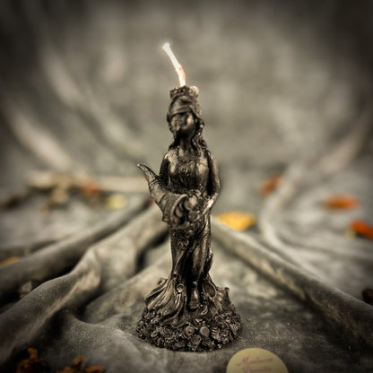 Statue of a woman holding a candle in a natural setting with blurred background