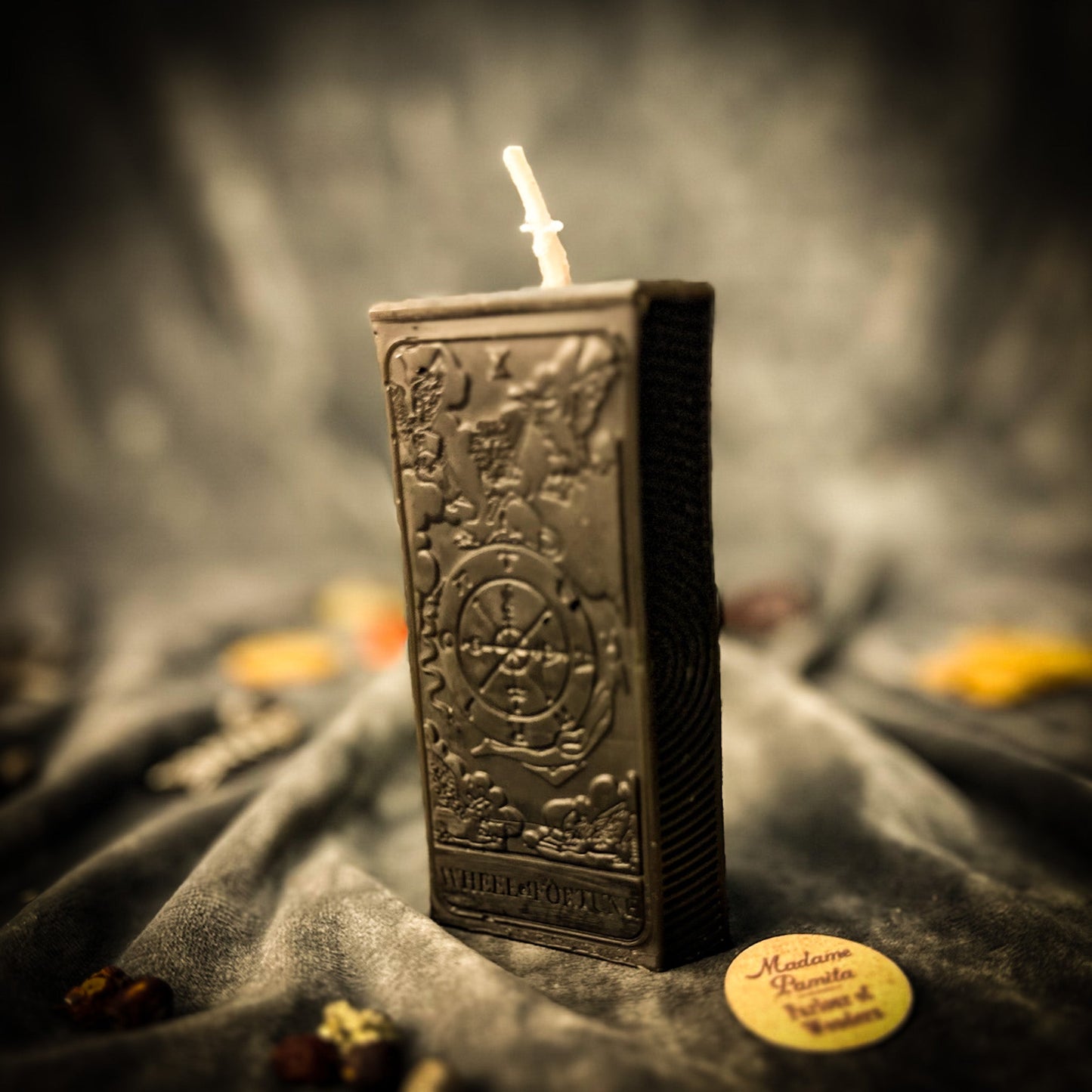 Decorative candle in a metallic container with intricate designs, on a dark fabric background.