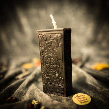 Decorative candle in a metallic container with intricate designs, on a dark fabric background.