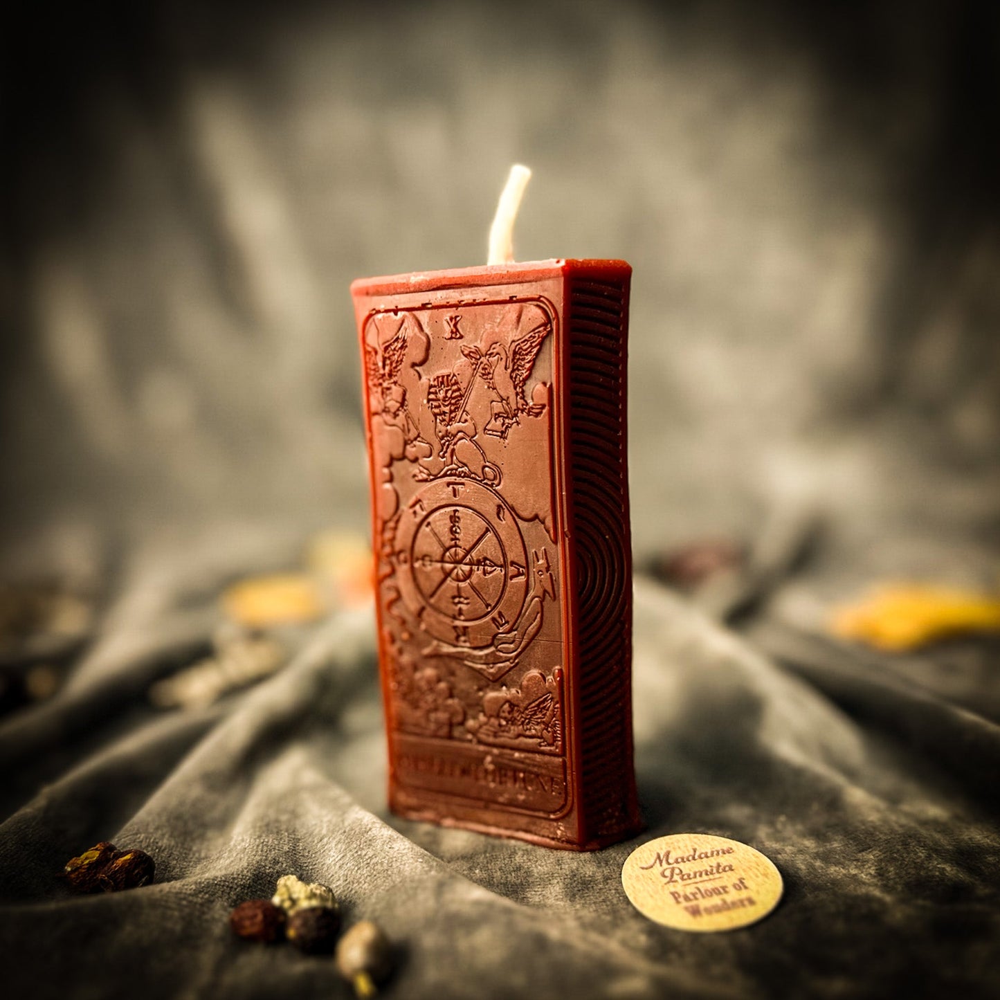 Red rectangular candle with intricate designs on a dark fabric background