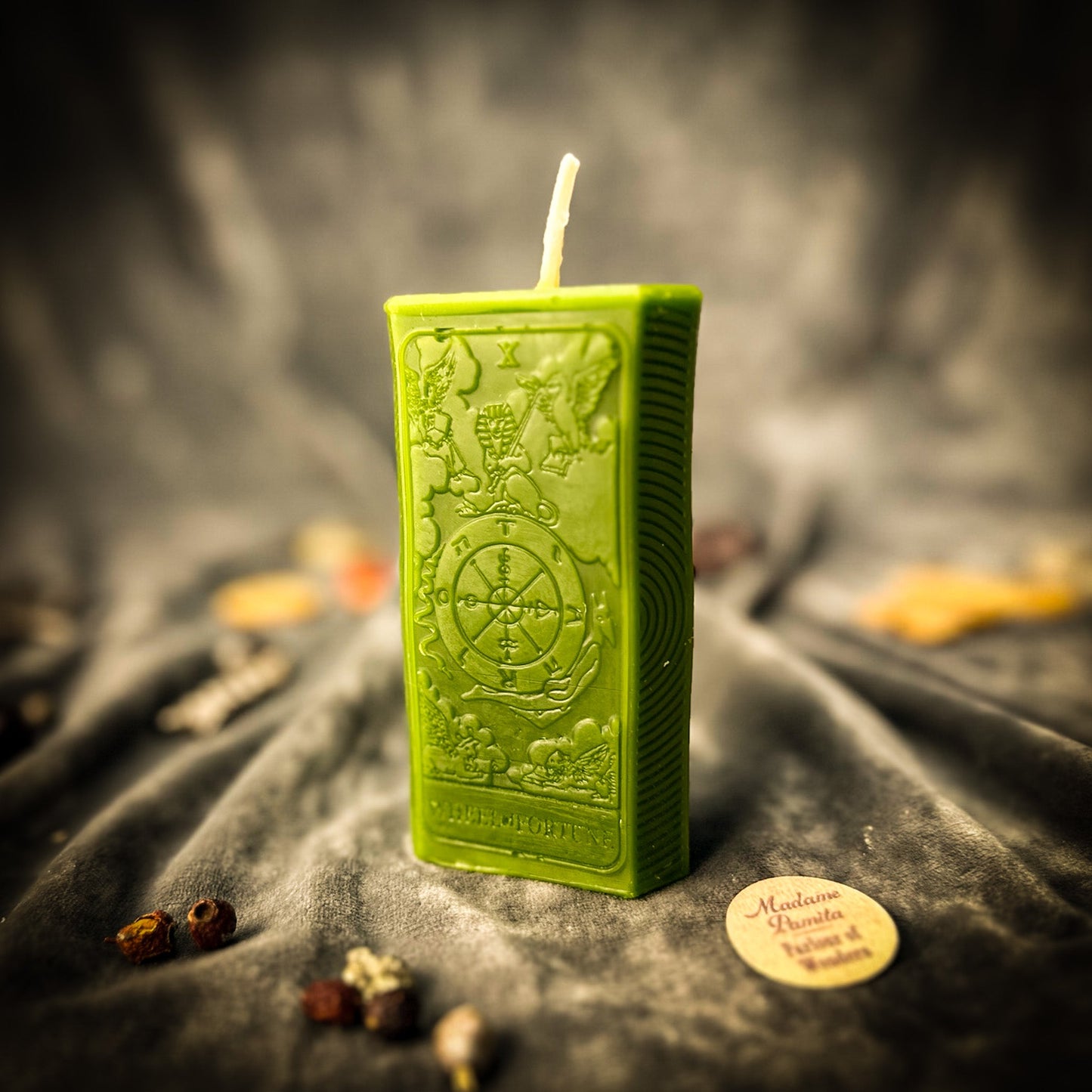 Green embossed candle on a dark fabric background with decorative elements