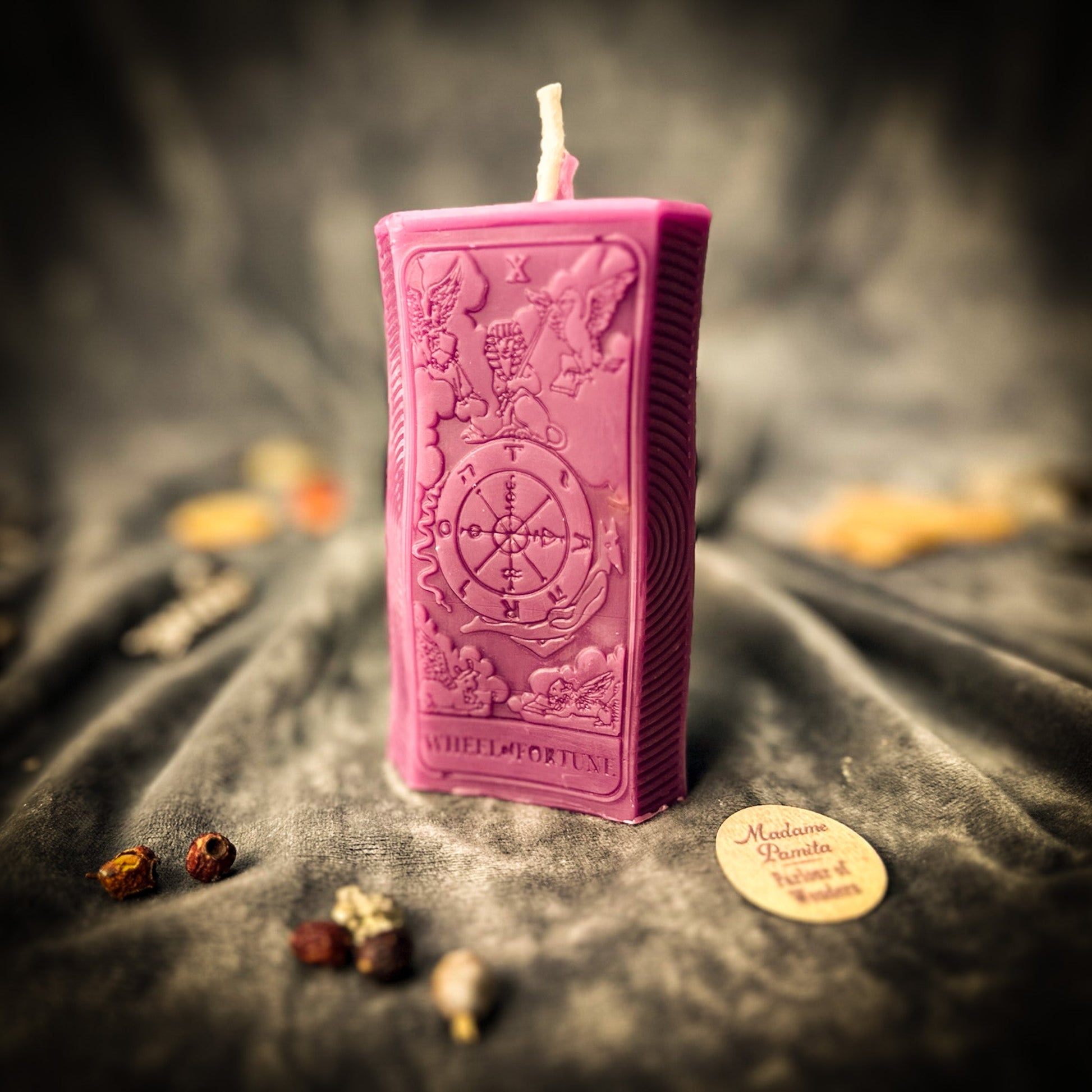 Pink rectangular candle with intricate designs on a dark fabric background