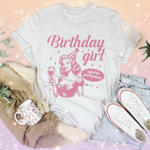 White t-shirt with pink 'Birthday girl' design on a white surface with casual items.