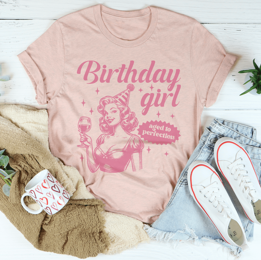 Pink t-shirt with 'Birthday girl' design on a white surface with accessories.