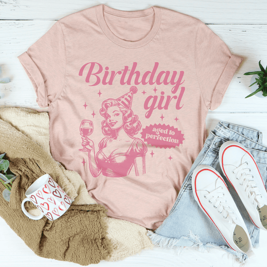 Pink t-shirt with 'Birthday girl' design on a white surface with accessories.