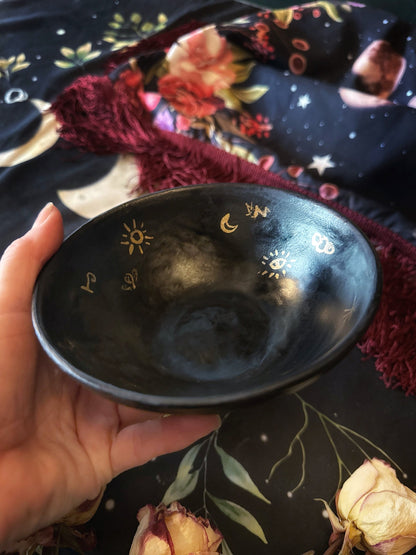Black bowl with celestial designs held by a hand against a decorative background
