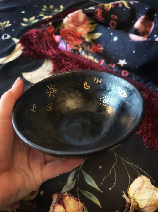 Black bowl with celestial designs held by a hand against a decorative background