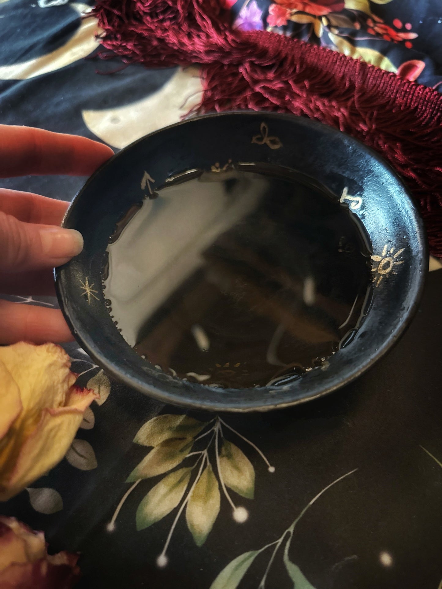 Black dish with gold patterns held by a hand on a floral fabric background