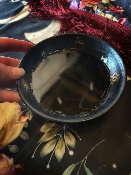 Black dish with gold patterns held by a hand on a floral fabric background