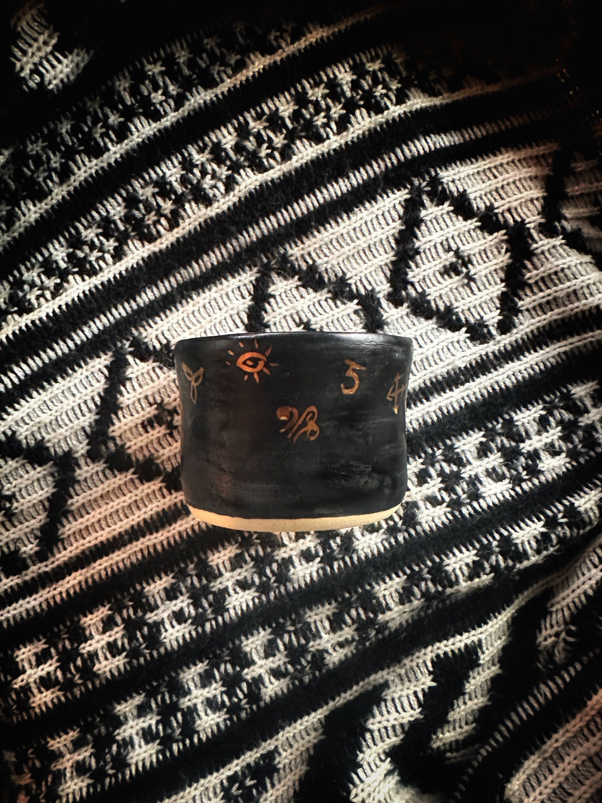 Black cylindrical container with decorative patterns on a patterned fabric background