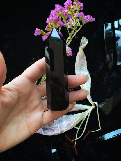Hand holding a black crystal with pink flowers in the background