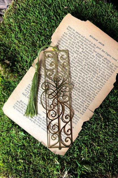 Decorative metal bookmark on an open book with a green moss background